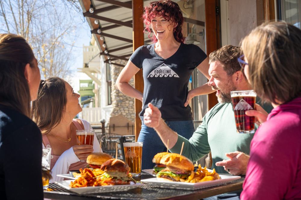 Server laughing with guests at a sunny window table