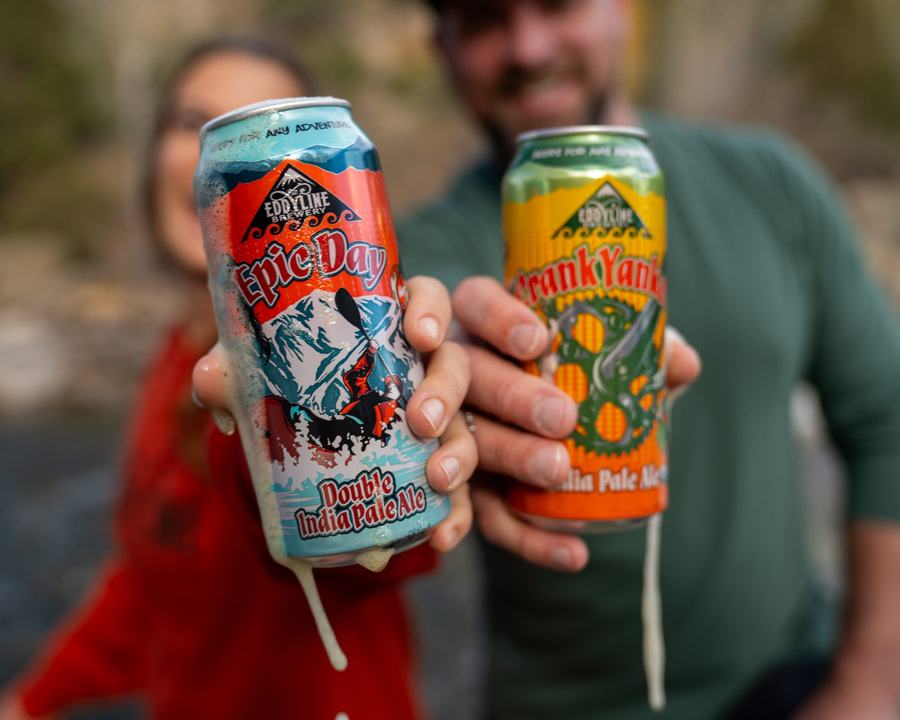 Two friends holding Eddyline Epic Day and CrankYanker cans by the river