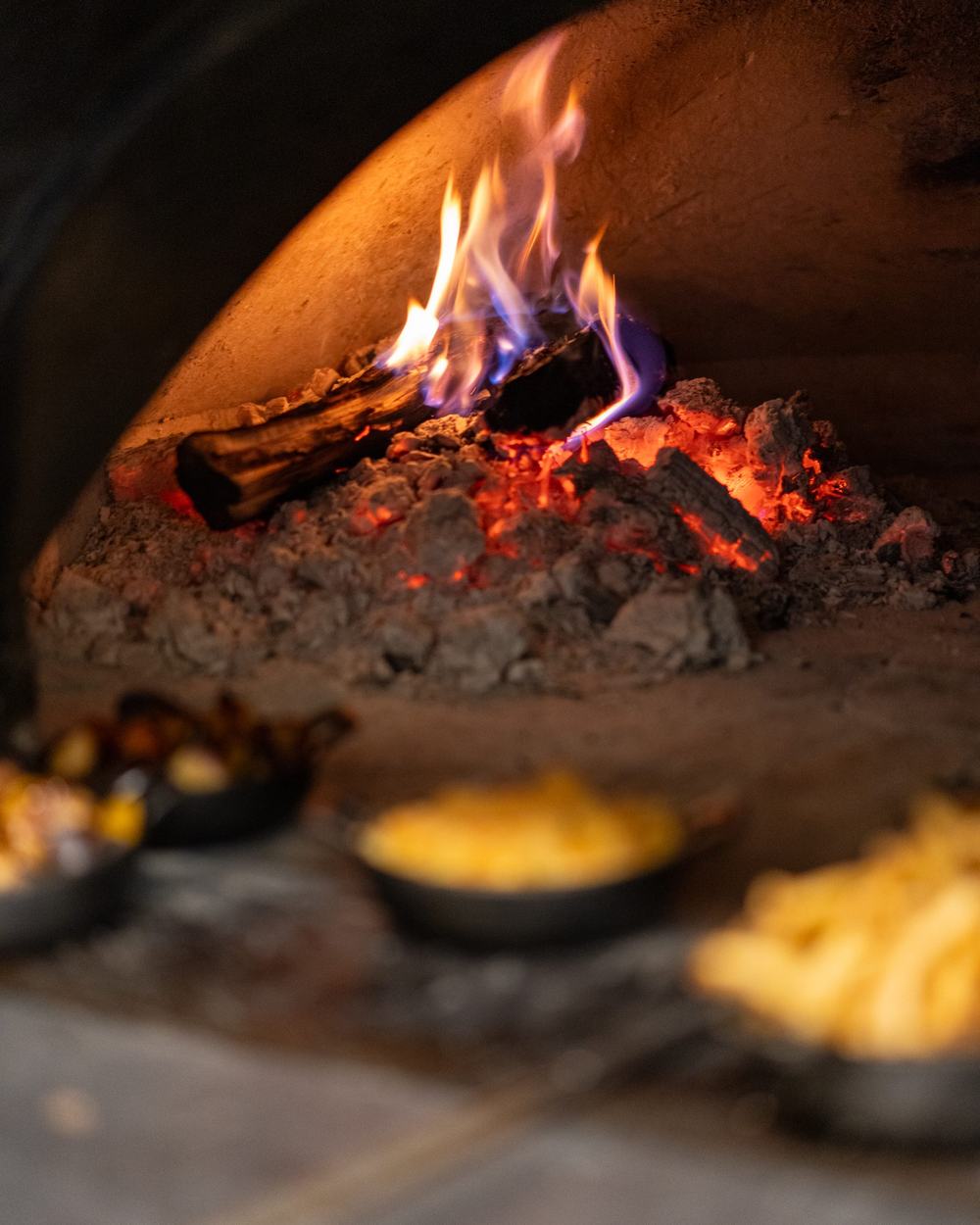 Open flame and cast iron pans inside the pecan wood-fired oven